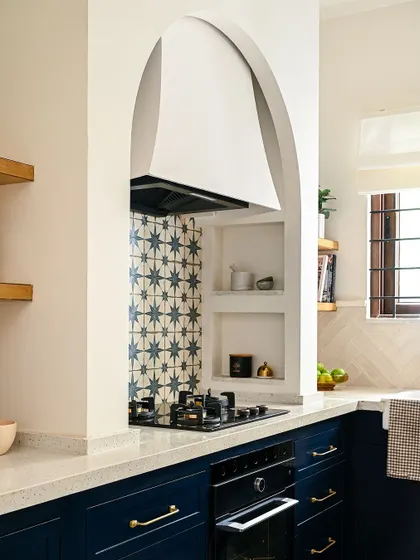 This close-up shows the custom arched chimney hood and the built-in nooks I designed to hold everyday cooking essentials. The patterned tile backsplash extends all the way to the ceiling, making a dramatic statement and adding a layer of beautiful detail to this Spanish-inspired kitchen design.