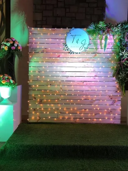 A rustic-chic photo booth created with a wooden pallet wall and fairy lights. We added a custom couple logo and some greenery to make it a personalized and charming spot for pictures.