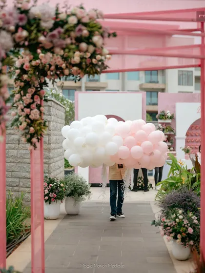A staff member carries bunches of pink and white balloons, adding to the light and airy party atmosphere.