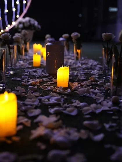The same romantic pathway seen at night. The candles create an even more intimate and magical atmosphere, with their warm light reflecting off the scattered petals.