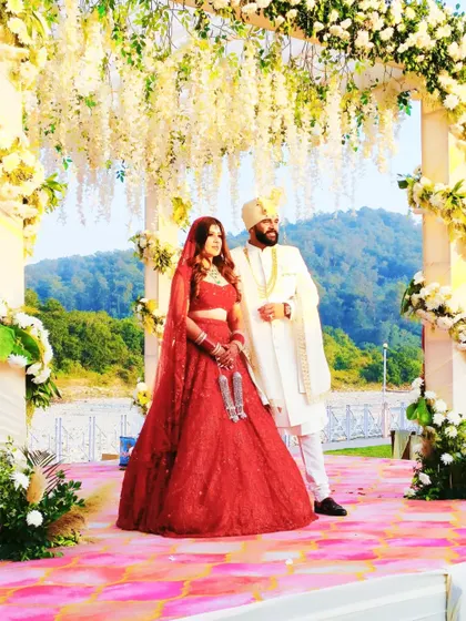 A beautiful couple stands on their wedding stage at a destination wedding in Jim Corbett, surrounded by a cascade of white flowers and a stunning natural view.