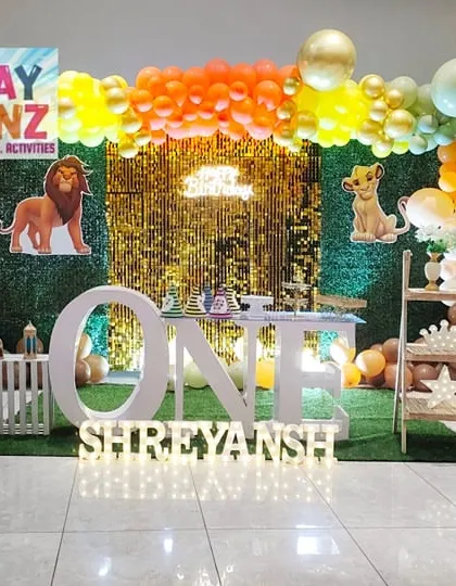 A Lion King inspired take on the classic jungle theme. This setup for a first birthday includes cutouts of Simba, Timon, and Pumbaa, a grass wall with a gold sequin center, and a personalized milestone board for baby Shreyansh.