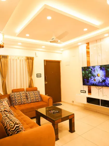 This living room features a floating TV console against a wall with marble and mirror panels. The false ceiling with cove lighting adds a warm, ambient glow to the entire room.