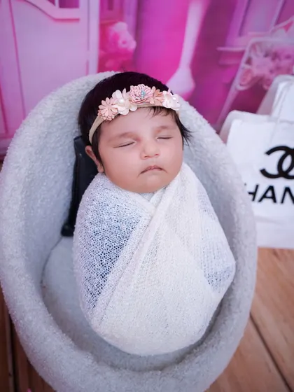 A detailed close-up of the newborn in the Chanel-themed shoot, showing her peaceful expression and the delicate floral headband.