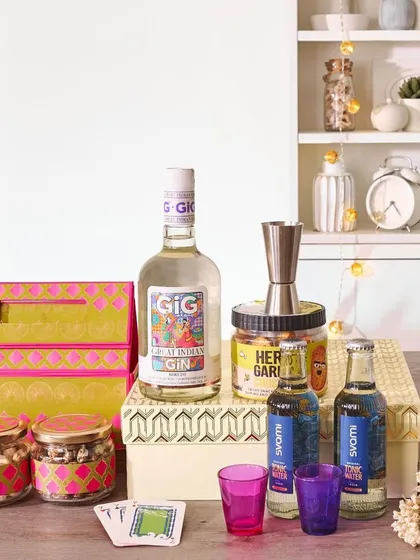 This modern gin-themed wedding hamper includes a bottle of Greater Than Gin, tonic water, a cocktail jigger, and snacks, all presented in vibrant, contemporary packaging.
