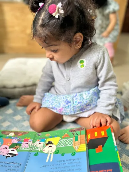 This toddler is completely absorbed in her book, a testament to how we nurture a love for reading from the very beginning.