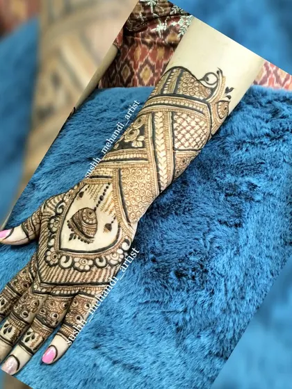 This design has a heart in the center with a kalash motif, surrounded by detailed patterns that extend to the wrist.