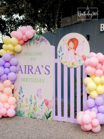 A welcoming entrance for Aira's fairy-themed birthday, featuring a custom sign, a whimsical picket fence, and a cascade of pastel balloons.
