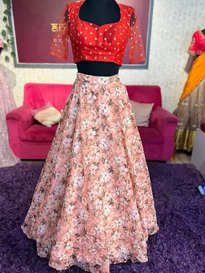 A mannequin displaying a lightweight floral lehenga paired with a bright red blouse with sheer, dotted sleeves.