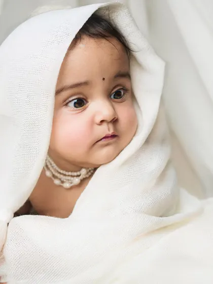 A baby wrapped in a soft white cloth, with only her curious face and a string of pearls visible. A simple, artistic, and incredibly sweet portrait.