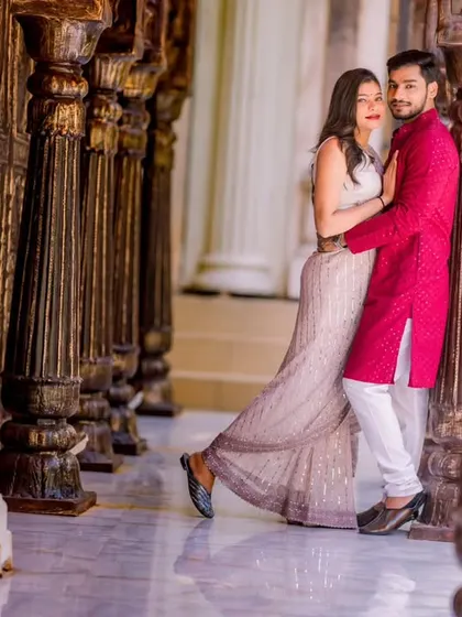 A stylish pose in a corridor of wooden pillars. The bride's elegant gown and the groom's traditional kurta create a beautiful fusion look.