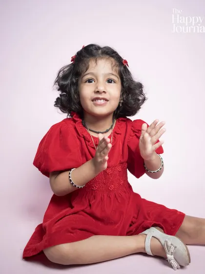 A little girl in a bright red dress, clapping her hands with a happy expression. This shot is full of life and joyful energy.