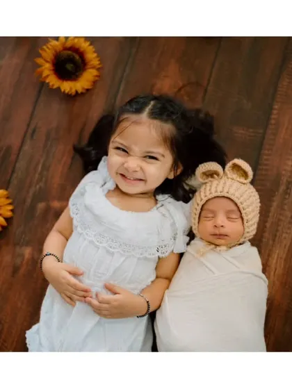 A moment of shared smiles between siblings. The older sister's playful expression and the baby's peaceful sleep create a beautiful contrast.