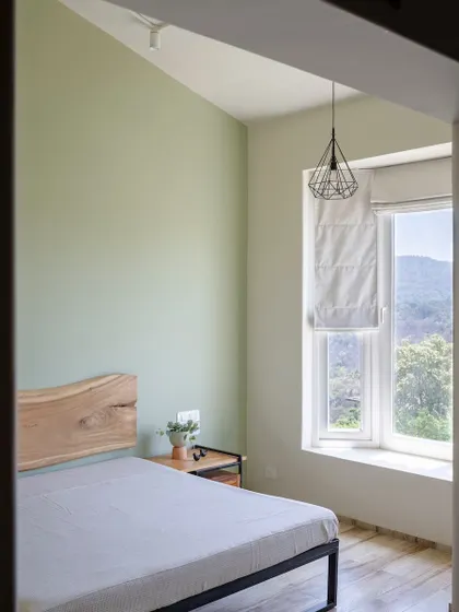 This bedroom uses a live-edge wood headboard as a natural, artistic focal point. The sage green wall and simple pendant light create a calm and soothing atmosphere, with the window offering a beautiful view of the hills.