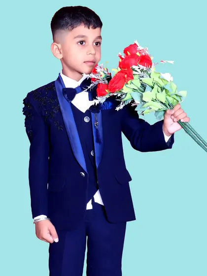 A dapper young boy in a full navy blue suit with a bow tie, holding a bouquet of flowers, ready for a special event or photoshoot.
