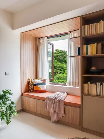 This image showcases a beautiful bay window seat, perfect for a child's reading nook. The built-in bookshelf and a view of the lush greenery outside make it a magical space.