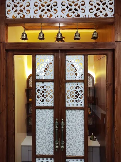 A close-up of the ornate door and the hanging brass bells, details that add an authentic and divine touch to the pooja room entrance.