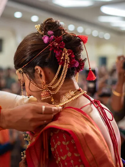 A candid shot from a wedding ceremony, focusing on the intricate bridal hairstyle with floral details and traditional jewellery.