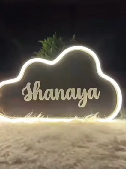 A warm white neon sign for "Shanaya," shown here on a soft, fluffy surface to highlight its cozy aesthetic.