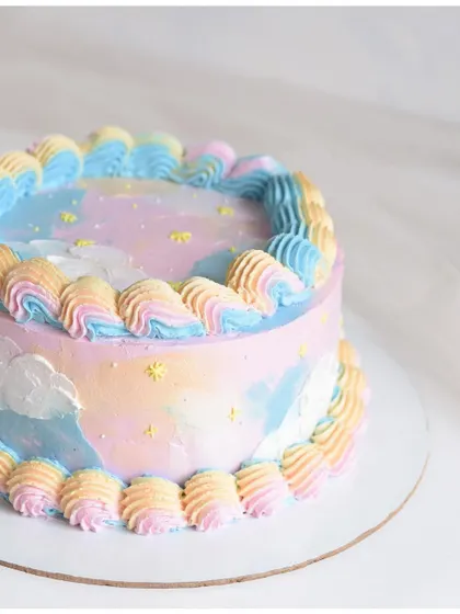 A dreamy pastel galaxy cake. The soft blend of pink, blue, and yellow creates a beautiful watercolor sky effect, complete with tiny stars and clouds.