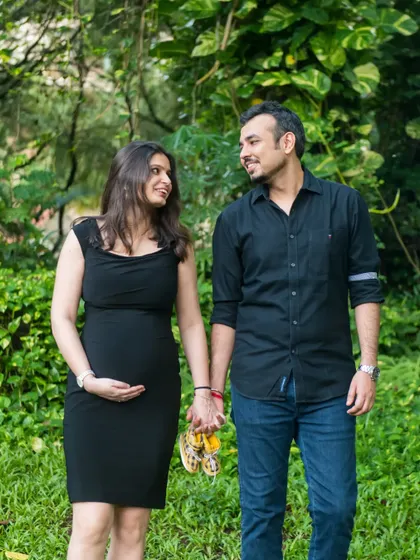 A classic walking shot in a park. The couple holds hands, carrying a pair of baby shoes, symbolizing the new path they are taking together as they await their child.