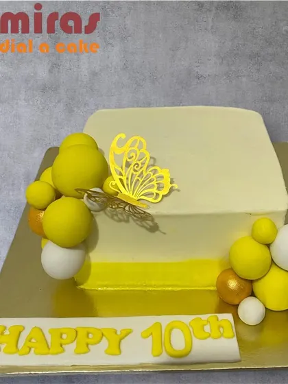 A chic and modern ombre cake for a 10th celebration. The square cake transitions from white to yellow and is decorated with spheres and a golden butterfly for a stylish touch.
