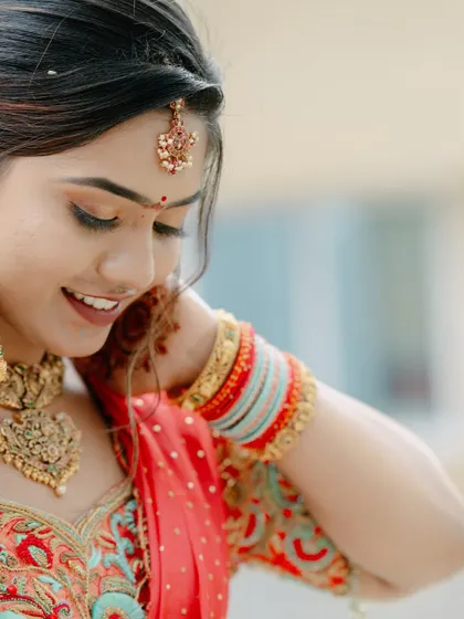 A candid, smiling portrait of a bride in a vibrant red lehenga, capturing a moment of genuine happiness.