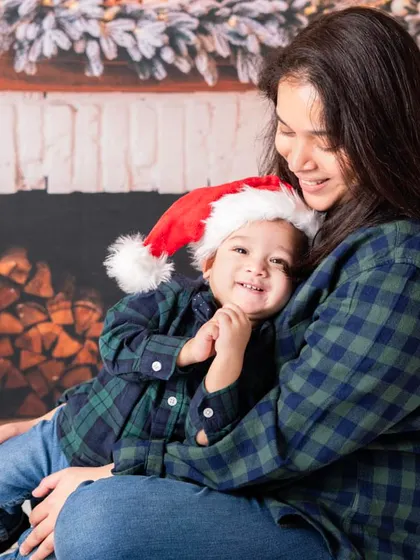 A candid moment between a mother and her baby during a Christmas shoot. The cozy flannel shirts and warm fireplace backdrop create a perfect holiday vibe.