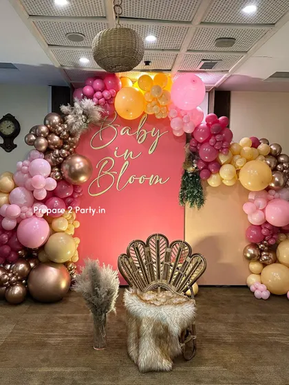 A full view of the "Baby in Bloom" setup, showing the balance of the balloon arch, the statement peacock chair, and the decorative pampas grass.