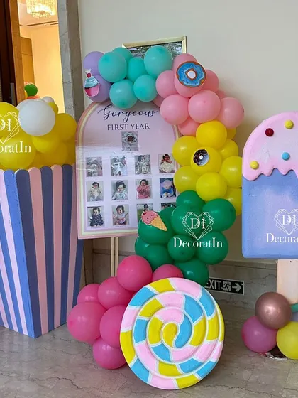A "Gorgeous First Year" milestone board displays monthly photos, surrounded by giant popcorn, lollipop, and ice cream props.