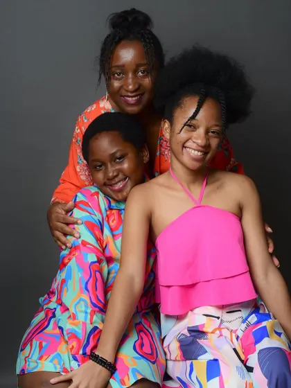 A vibrant portrait of a mother and her two daughters. Their colorful outfits and bright smiles make this a joyful family photo.