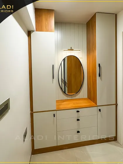 A clean and minimalist entryway unit featuring a combination of white and wood-finish cabinets, drawers, and an oval mirror with a picture light.