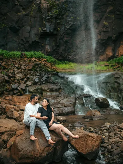 A romantic moment as a couple sits on the rocks by a waterfall.