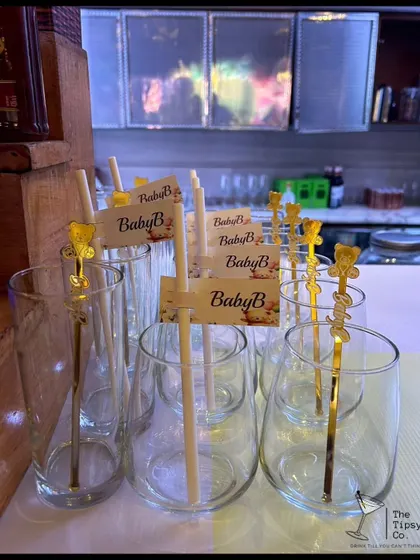 Personalized glassware ready for a baby shower. The custom "Baby B" tags and gold stirrers show how we tailor every detail to the specific event.