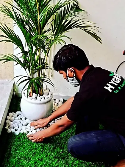 A close-up of my work on a balcony garden. I'm adding decorative white pebbles to a potted Areca palm set on artificial turf, creating a clean and stylish look.