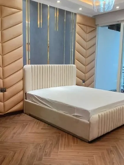 A premium bedroom featuring a fully upholstered bed and a cushioned, chevron-patterned accent wall. The design exudes subtlety and luxury, with a view of the city from the balcony.