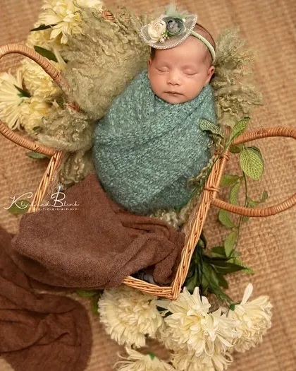 A basket full of precious moments. This newborn is wrapped in a lovely teal swaddle and placed in a basket, surrounded by soft textures and white flowers.