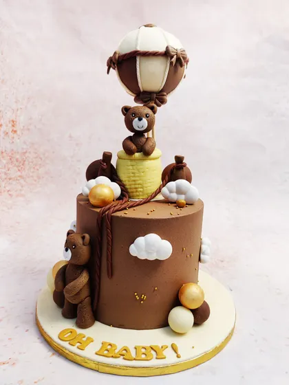 We take to the skies with this charming teddy bear hot air balloon cake. This "Oh Baby!" themed cake features adorable teddy bears on a chocolate-frosted tier, with one bear soaring high in a meticulously crafted hot air balloon.