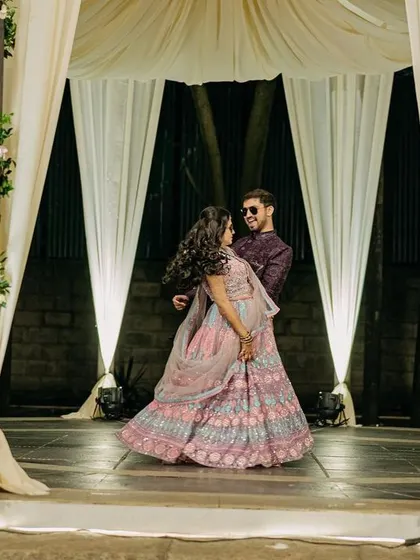 A couple shares a dance on the beautifully lit sangeet stage, with elegant white drapes creating a soft and romantic backdrop.