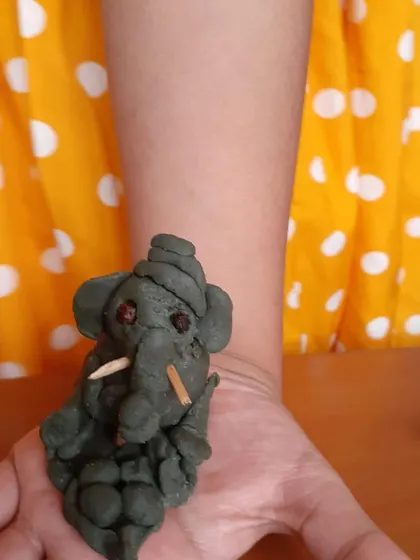 A simple yet expressive Ganesha made from clay, held in the palm of a child's hand.