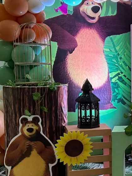 A detail shot from a Masha and the Bear themed party. This image shows a large cutout of the Bear character against a jungle backdrop with themed props like a lantern and birdcage.