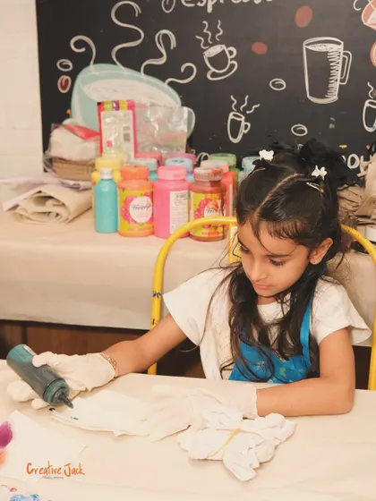 A young girl in a blue apron is focused on a tie-dye project, carefully applying color to the fabric during a birthday workshop.