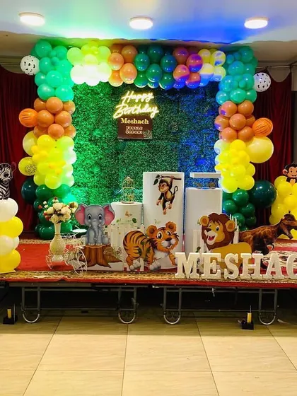 This jungle theme is set up on a stage, making it the central focus of the party. It features a grass backdrop, a neon sign, and character cutouts like a tiger, lion, and monkey.