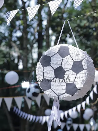 A soccer ball piñata hanging at an outdoor party. This fun activity, along with the black and white checkered bunting, adds to the sporty and interactive atmosphere of the event.