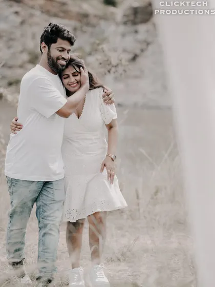 A happy, full-body shot of a couple embracing in a field, framed by a white curtain, capturing a candid and loving moment.