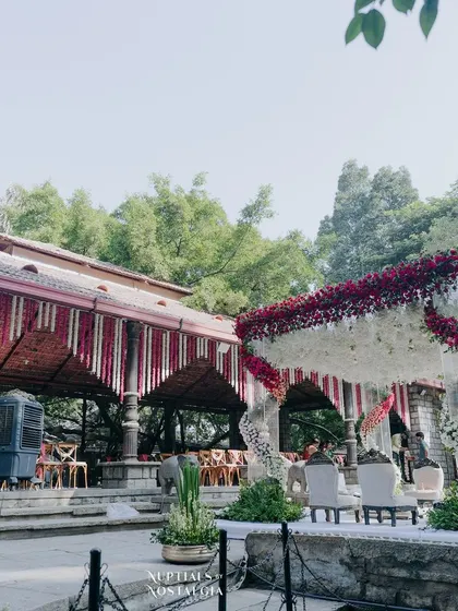The wedding mandap and guest seating area, decorated with complementary floral themes. The red and white of the mandap are echoed in the decor throughout the venue, creating a cohesive and elegant look.