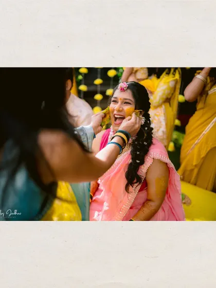 A candid moment of the bride laughing as her friends apply Haldi.