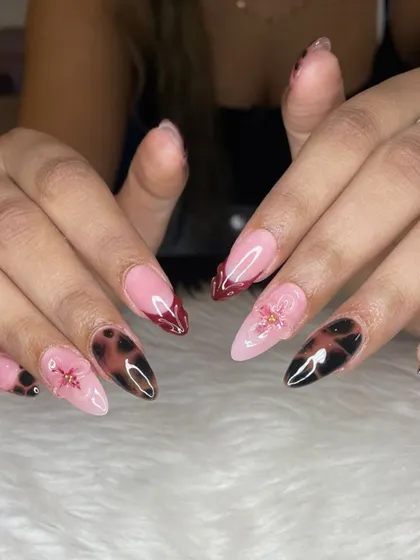 For when you're feeling moody and glam. This set features a mix of trendy tortoise shell nail art, deep red French tips, and delicate 3D floral accents on sharp stiletto extensions.