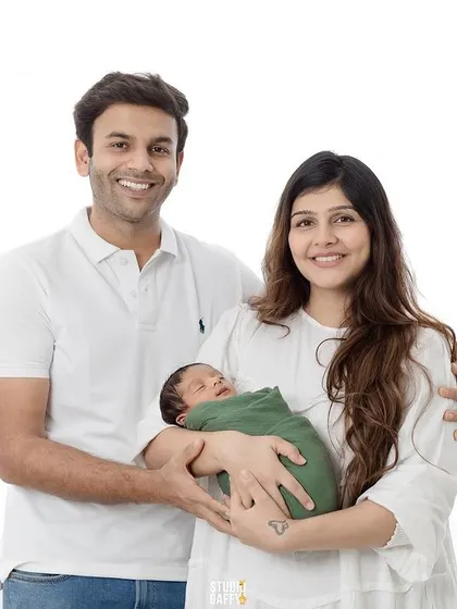 A classic first family portrait, with both parents smiling brightly as they hold their new baby.