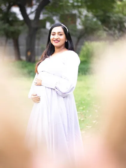 This is a creative and heartfelt shot, framed by the father-to-be's hands making a heart shape. It beautifully centers the expecting mother and her bump, symbolizing that she is the heart of their growing family.